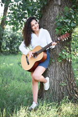 young woman walking in the forest and playing guitar, summer nature, bright sunlight, shadows and green leaves, romantic feelings