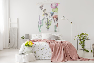 Fototapeta A bunch of yellow fresh cut flowers in a bright bedroom interior with a bed dressed in white linen and peach blanket. Fabric on the wall above the bed. Real photo. obraz