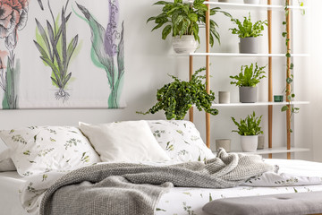 Urban jungle bedroom interior with plants in pots beside a bed dressed in organic cotton linen of white color with green print. Real photo.