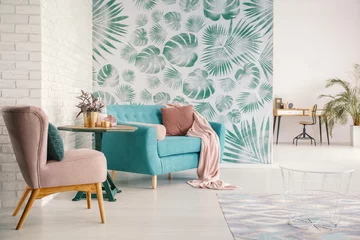 Fotobehang Flowers on table between pink armchair and turquoise sofa in flat interior with green wallpaper. Real photo © Photographee.eu