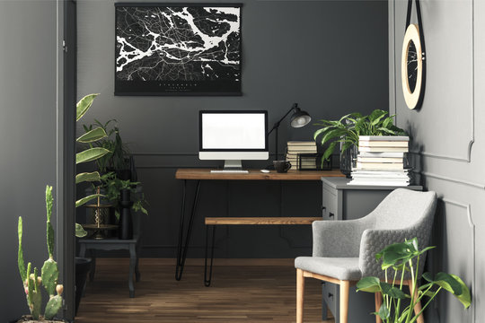 Painting above desk with mockup of computer desktop in grey workspace interior with armchair. Real photo