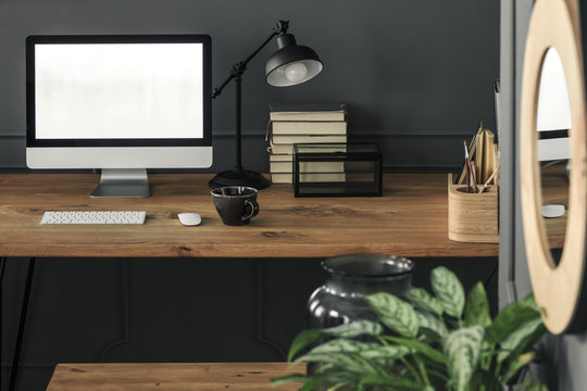 Mockup on computer desktop on wooden desk with lamp in grey work area interior. Real photo