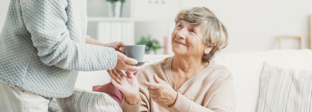 Close-up of person with cup of tea taking care of smiling senior woman