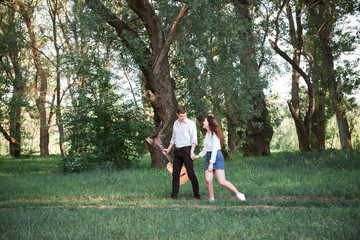 young couple walking in the forest and playing guitar, summer nature, bright sunlight, shadows and green leaves, romantic feelings