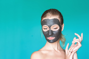 Beauty portrait of a woman with a black mask on her face against a blue turquoise background