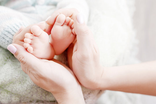 Newborn baby feet in mother hands, shape like a lovely heart. Mother holding legs of the kid in hands. Close up image. Happy family concept.