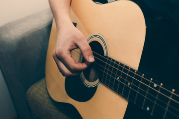 Man at home is playing the guitar. Guys hands are taking the chord on strings. Music making...