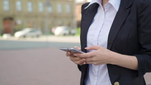 Close-up shot of female hands typing sms or chat message on smart phone at the outside.