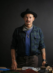 Portrait of young leather artisian posing near workplace with scobbler tools at his workshop