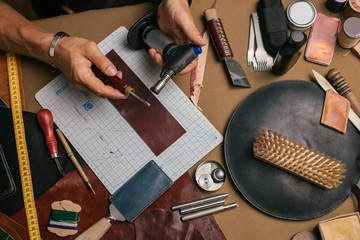 A close-up of a man skinner makes leather pattern with the help of a special knife in the workshop. Leather Craftsman manufactures a custom made pocketbook.