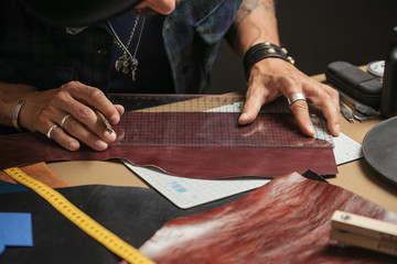 Skilled professional shoemaker making custom made leather wallet from genuine leather samples at a workshop, close up high angle shot.