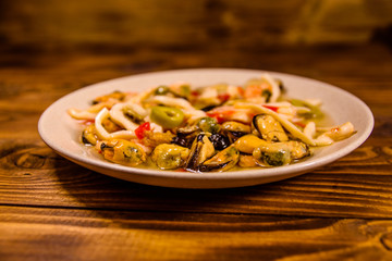 Ceramic plate with different sea food and olives on wooden table