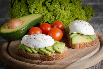 Avocado toast, cherry tomato and poached eggs on wooden background. Breakfast with vegetarian food, healthy diet concept.