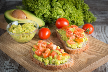Avocado toast, cherry tomato and poached eggs on wooden background. Breakfast with vegetarian food, healthy diet concept.