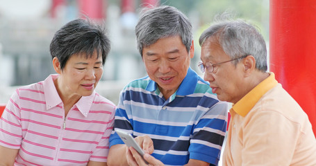 Senior old friends looking at mobile phone together at outdoor