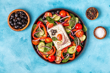 Fototapeta na wymiar Greek salad of fresh cucumber, tomato, sweet pepper, spinach, red onion, feta cheese and olives