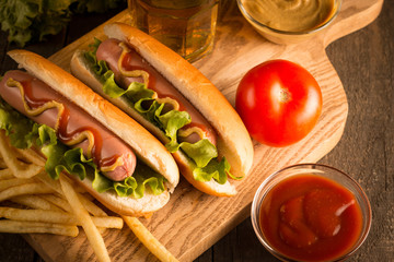 Photo of barbecue grilled hot dog with yellow mustard and ketchup on wooden background. Hot dog sandwich with potato fries and sauces.