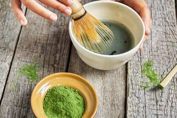 Matcha green tea accessoires on the rough wooden boards with girl's hands preparing matcha tea in a clay bowl