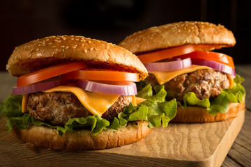 Home made hamburger with beef, onion, tomato, lettuce and cheese. Fresh burger close up on wooden rustic table with potato fries, beer and chips. Cheeseburger.