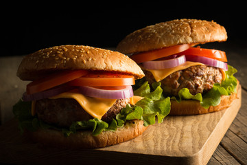 Home made hamburger with beef, onion, tomato, lettuce and cheese. Fresh burger close up on wooden rustic table with potato fries, beer and chips. Cheeseburger.