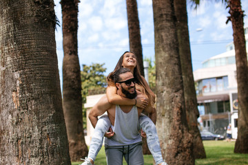 Happy sportive man in love giving piggyback ride to smiling woman at tropical trees park. Couple enjoying vacation at luxury hotel with copy space. Banner of summer young couple in a tropical country