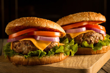 Home made hamburger with beef, onion, tomato, lettuce and cheese. Fresh burger close up on wooden rustic table with potato fries, beer and chips. Cheeseburger.