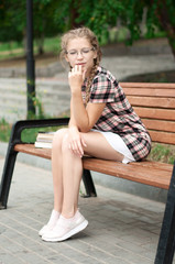 cute girl with glasses and in short dress sit dreamily on bench