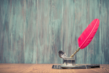 Quill ink pen with old inkwell on oak desk front aged grunge wooden textured background. Vintage old style filtered photo