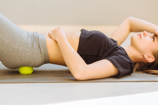 Close up of female doing self-massage technique applying tennis balls for back pain relief, working out on fitness mat on grey studio floor background, closeup.
