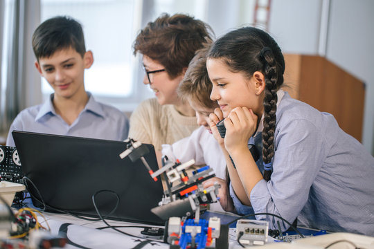 Curious smart caucasian pupils kids with female teacher enjoying science robotics lessons in technical school using laptop, study programming skill