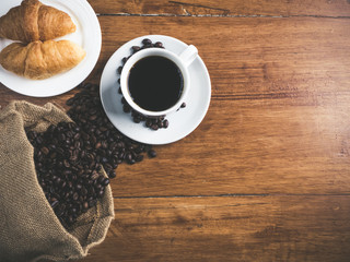 Coffee is a brewed drink prepared from roasted coffee beans, Coffee cup, coffee beans and croissant on a wooden table