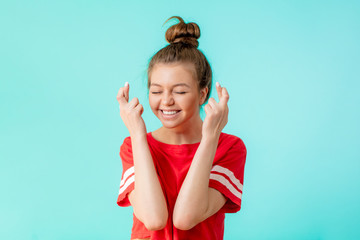 glad happy woman wears red t-shirt, keeps fingers crossed, hopes for good luck, isolated on blue...