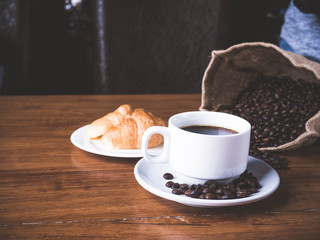 Coffee is a brewed drink prepared from roasted coffee beans, Coffee cup, coffee beans and croissant on a wooden table