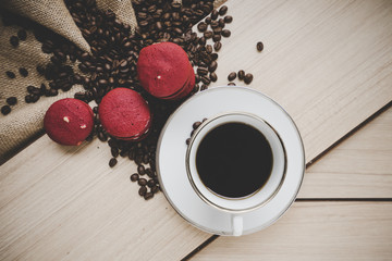 Coffee beans on burlap sack with coffee cub and red macaron on wood background, Top view.