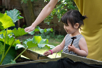 Naklejka na ściany i meble Cute child girl helps her mother in the garden. Mother and daughter in the backyard taking care of plants. Time together