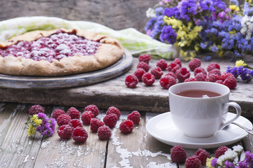 The cup of fresh tea with homemade biscuit of fresh natural raspberries and flowers on a wooden table.