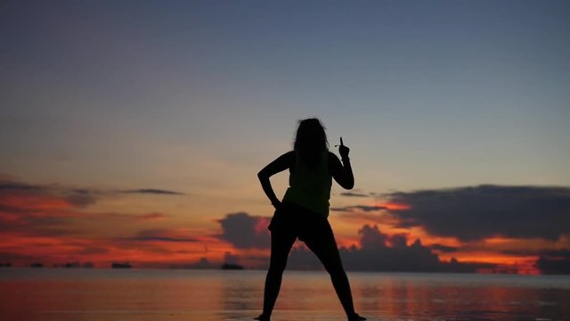 The chic girl is pleased with the sunset, stands on the beach in the water and dances, the movement of the camera. slowmotion, HD, 1920x1080