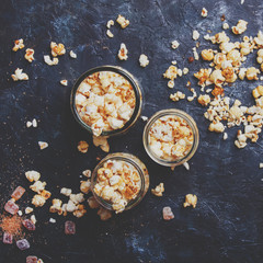Caramel sweet popcorn in glass jars on dark background, top view