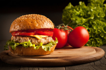 Home made hamburger with beef, onion, tomato, lettuce and cheese. Fresh burger close up on wooden rustic table with potato fries, beer and chips. Cheeseburger.