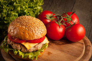 Home made hamburger with beef, onion, tomato, lettuce and cheese. Fresh burger close up on wooden rustic table with potato fries, beer and chips. Cheeseburger.