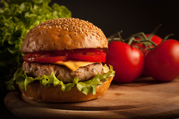 Home made hamburger with beef, onion, tomato, lettuce and cheese. Fresh burger close up on wooden rustic table with potato fries, beer and chips. Cheeseburger.