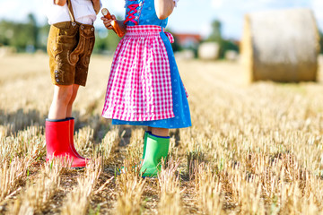 Two kids in traditional Bavarian costumes and red and green rubber boots in wheat field. German...