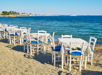 Fototapeta na wymiar A table with chairs of a greek tavern near the sea in a beach of Kos island, Greece.
