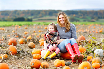Little kid girl and beautiful mother having fun with farming on a pumpkin patch. Traditional family...
