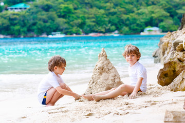 Two little kids boys having fun with building a sand castle on tropical beach of Seychelles. children playing together on their vacations