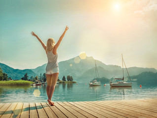 Happiness blonde woman stay on the wooden pier near the mountain