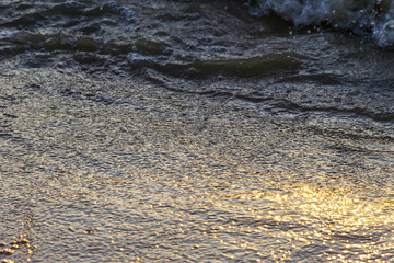 Waves on the sandy shore of a large river. The rays of light are reflected in the waves.