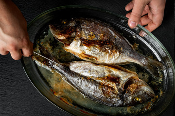 Baked sea fish with seasoning in baking pan on wooden table background.