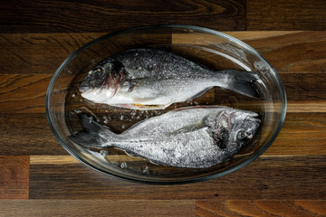 Fresh sea fish recipe with seasoning vegetables in baking pan on wooden table, copy text menu.