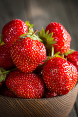 Macro photo of fresh ripe red strawberry in a wooden bowl on rustic background. Organic natural products.